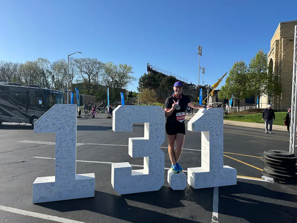 Runner celebrating with 13.1 marker, outdoor event.