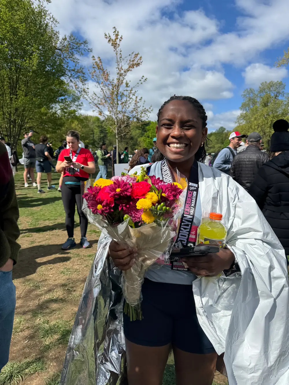 Smiling runner holding flowers and drink after race.