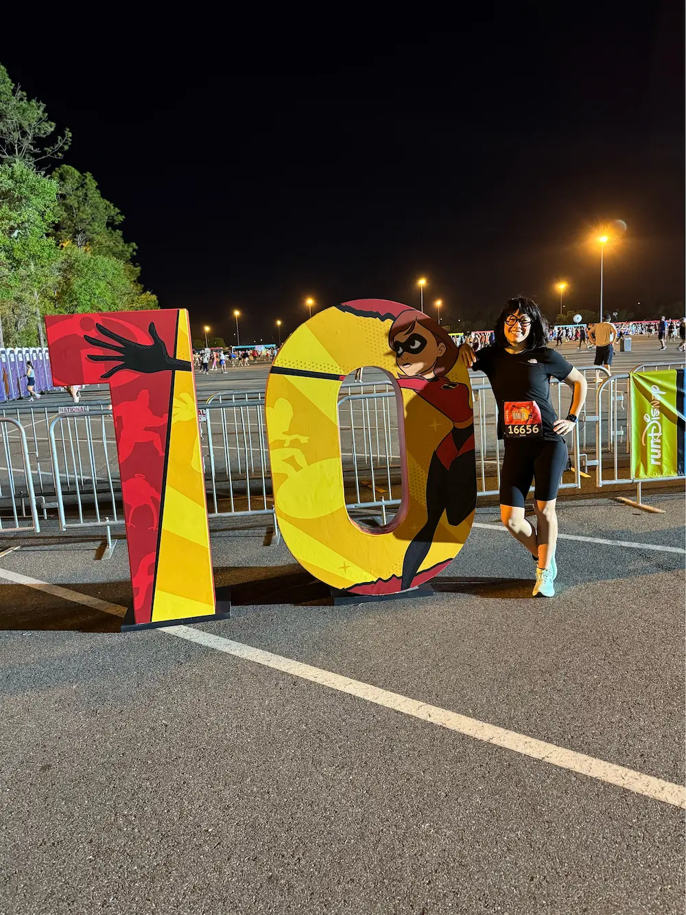 Woman poses with large '10' race sign at night.