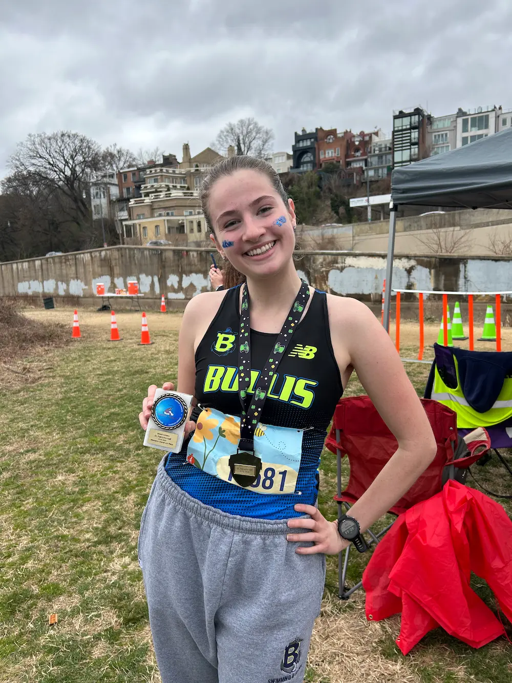 Runner smiling with medal at outdoor event.