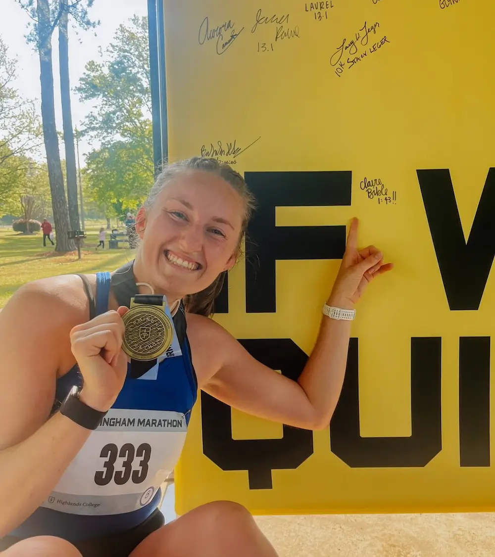 Smiling marathon runner with medal, pointing at sign.