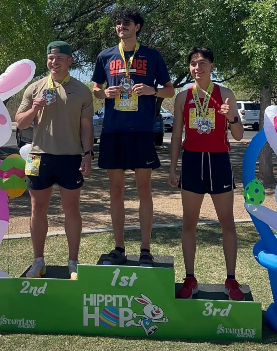 Three runners on podium with medals after race.