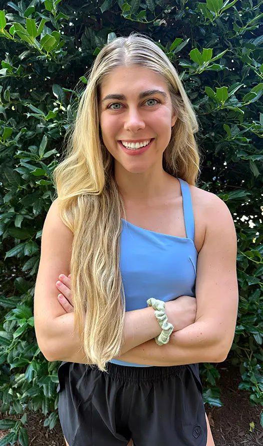 Smiling woman standing in front of green foliage.