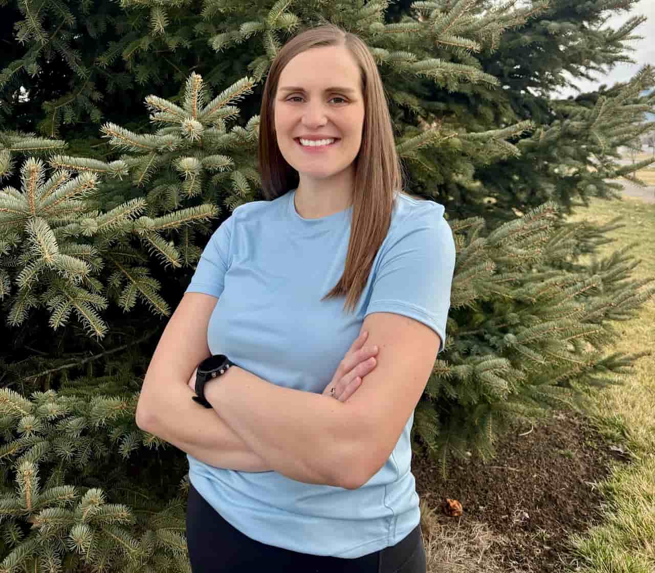 Smiling person standing in front of pine tree.
