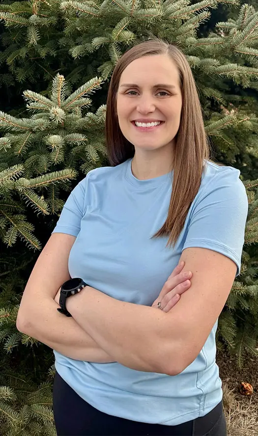 Smiling person standing in front of pine tree.